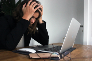 A Visibly Distressed Woman Holding Her Head While Staring at Something on Her Laptop Screen