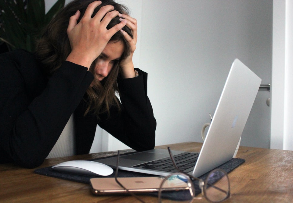 A Visibly Distressed Woman Holding Her Head While Staring at Something on Her Laptop Screen
